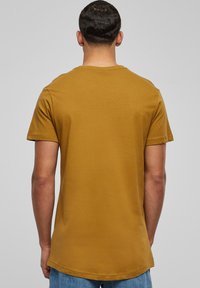 Kortærmet T-shirt i sennepsgul, med rund hals og lige snit. Glat bomuldsstruktur med et ensfarvet design, uden mønstre.