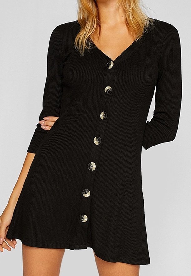 Femme portant une robe noire moulante en maille côtelée avec des manches longues, un décolleté en V et une rangée de gros boutons sur le devant.