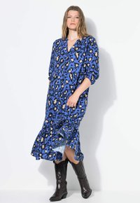 Abito blu con fantasia leopardata, scollo a V, maniche lunghe e orlo arricciato. Realizzato in tessuto leggero, abbinato a stivali in pelle marrone al ginocchio.