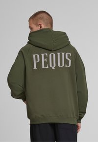 Sudadera con capucha de color verde oliva con un ajuste oversized. Presenta un gran texto "PEQUS" en gris claro en la parte de atrás y puños y dobladillo acanalados.