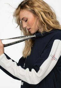 Marine hoodie med hvide ærmer og logo. Har snøre med branding og ankerdesign. Blødt stof med afslappet pasform og lange ærmer.