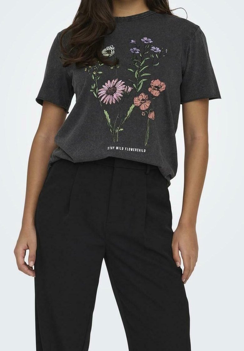 Femme portant un pantalon noir taille haute et un T-shirt gris foncé avec une illustration florale en rose, violet et orange et le texte "STAY WILD FLOWERCHILD".