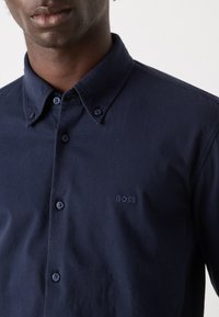 Marineblauwe katoenen overhemd met knopen, voorzien van een kraag, twee knopen en een geborduurd "BOSS" logo op de borst. Soepele textuur.