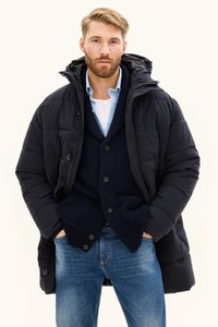 Czarna kurtka puchowa z kapturem, z zamkiem z przodu i guziczkami, nakładana na granatowy sweter wykonany na drutach. Pod spodem jasnoniebieska koszula.