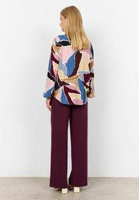 Colorful blouse with abstract leaf patterns in pink, blue, and brown, paired with wide, deep burgundy pants and light-colored block heels.