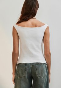 Vit, åtsittande linne med vid halsringning och korta ärmar, tillverkat av slät tyg. Ovanpå höga midjebyxor i denim.