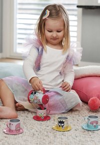 Leikkikuppisarja, jossa on vaaleanpunaisia, sinisiä ja keltaisia kuppeja ja aluslautasia, joissa on sarjakuvahahmoja. Tyttö kaataa punaisesta teekannusta kuppiin.