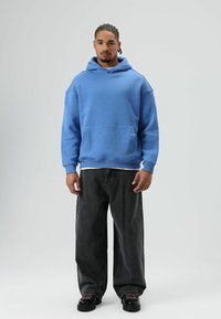 Lichtblauwe katoenen hoodie met een buidelzak, gecombineerd met oversized donkergrijze spijkerbroek en zwarte veterlaarzen.