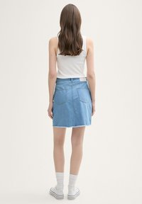 Leren denim rok in lichtblauw met een rafelige zoom. Bevat twee achterzakken en een taille label. Gecombineerd met een witte tanktop en witte sokken.
