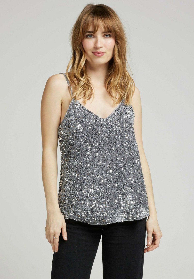 Débardeur en sequins argentés avec bretelles spaghetti réglables ; design en V ; surface brillante et texturée ; coupe ample ; associé à un pantalon noir.