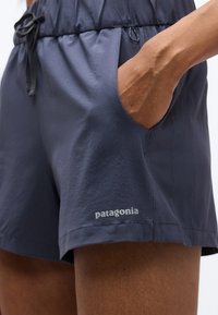 Κοντινή λήψη ενός ατόμου που φοράει σκούρο μπλε σορτς Patagonia με το χέρι στην δεξιά τσέπη και μαύρο κορδόνι στη μέση.