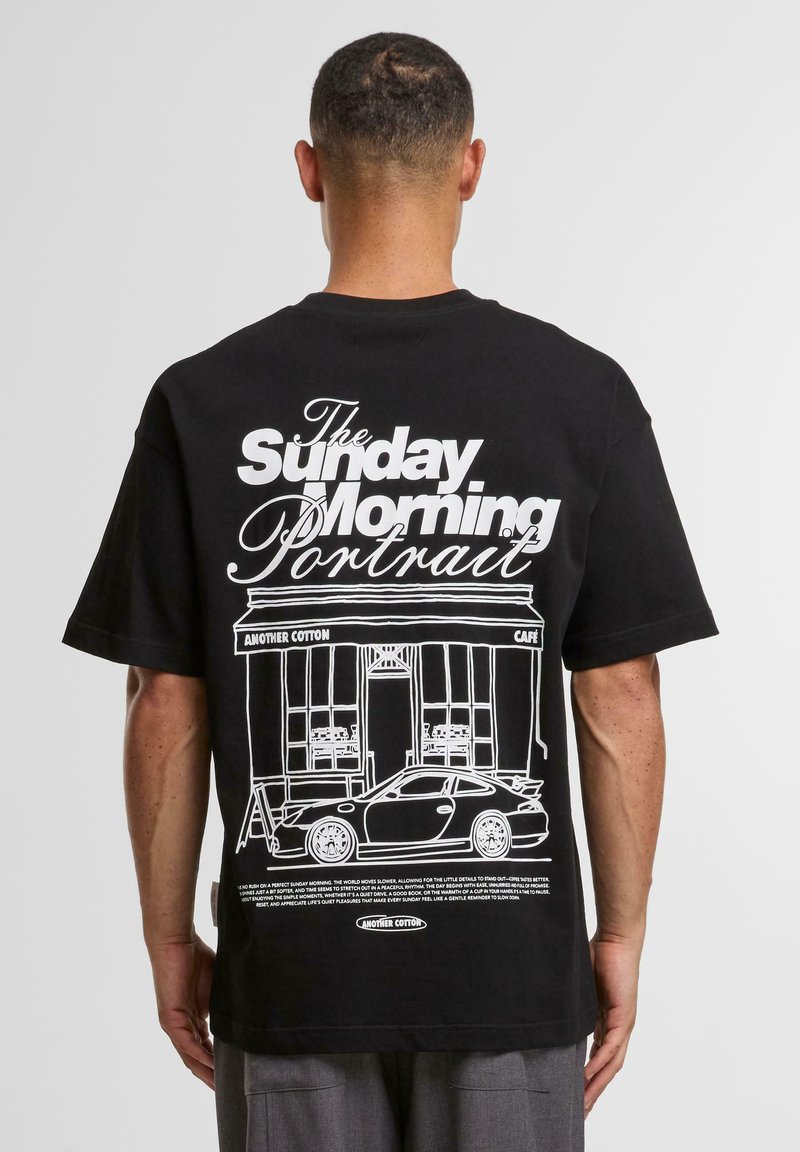 Tricou negru din bumbac, cu un design grafic alb pe spate, reprezentând o cafenea și o mașină, cu un text îndrăzneț deasupra ilustrației.