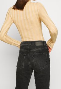 Top a maniche lunghe in beige chiaro a coste con righe verticali, abbinato a jeans neri a vita alta con una patch in pelle e due tasche posteriori.