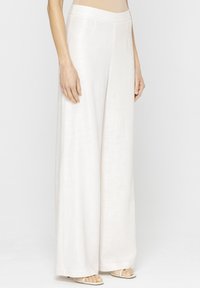 Szerokie spodnie wykonane z lekkiego, teksturowanego materiału w jasnym odcieniu kremowym. Posiadają gładki, płaski pas. W zestawie z prostymi, lekkimi sandałami.
