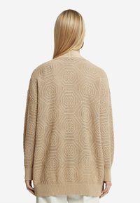 Stickad kofta i ljusbeige med hexagonmönster, lös passform, långa ärmar och ribbade mudd och fåll. Strukturerad yta tydlig.