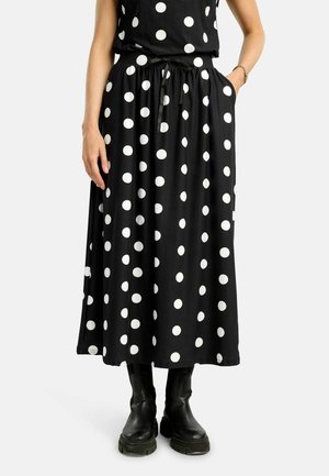 Donna che indossa una gonna midi nera con grandi pois bianchi, abbinata a stivali neri robusti e un top nero senza maniche.