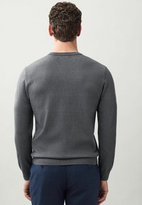Jersey gris de punto con cuello redondo y mangas largas, que presenta una textura suave y puños y dobladillo acanalados.