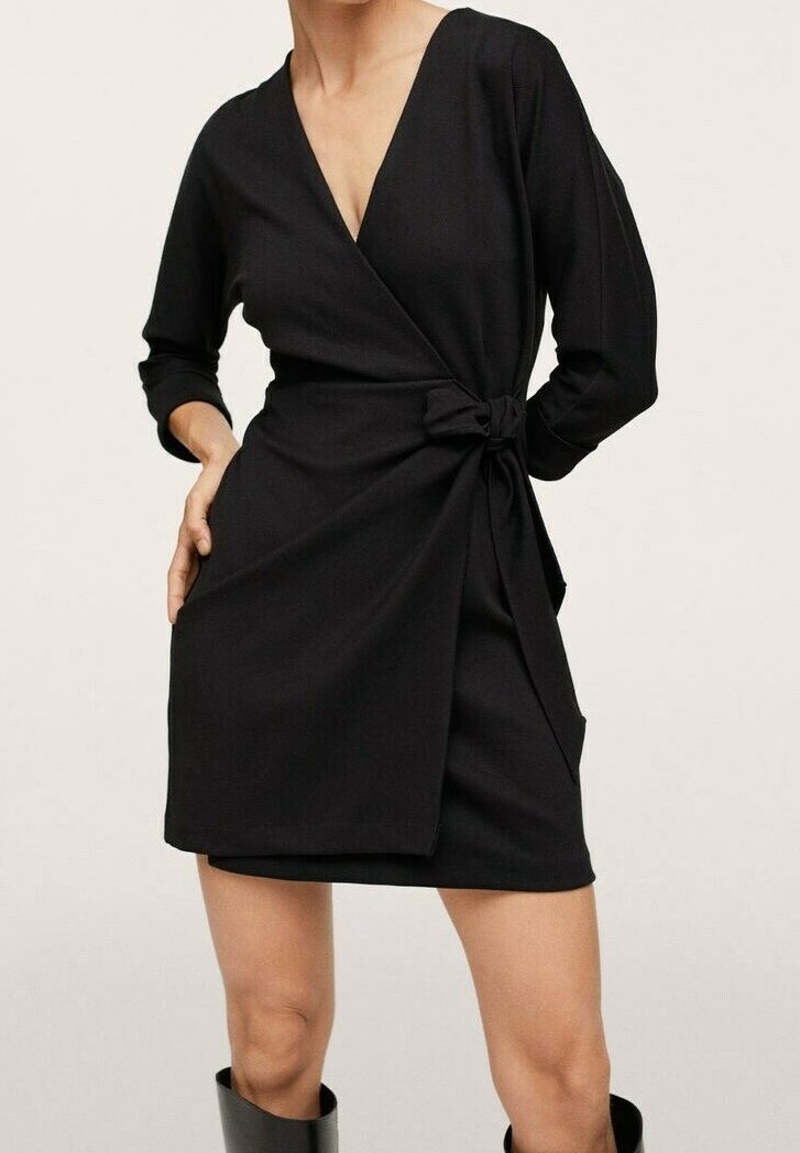 Femme portant une robe portefeuille noire à manches trois-quarts nouée à la taille, associée à des bottes noires montantes au genou.