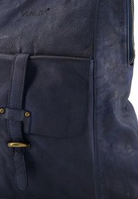 Granatowy skórzany plecak z teksturowanym wykończeniem, z przednią kieszenią zabezpieczoną paskiem i mosiężnymi akcentami.