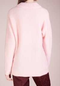 Rosa oversized tröja i mjukt, fluffigt material, med ribbat krage och ärmslut, av avslappnad passform och sänkta axlar.