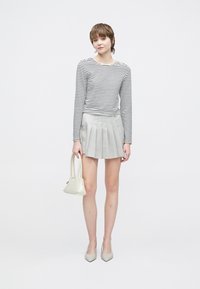 Pasiasty top z długim rękawem, szara plisowana spódnica, jasna torebka i czółenka na szpilce. Czyste linie i neutralne kolory tworzą nowoczesny wygląd.