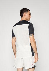 Czarny i biały sportowy T-shirt z siateczkowym tyłem, krótkimi rękawami i okrągłym dekoltem, w komplecie z jasnymi szortami.