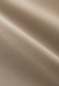 Tissu beige lisse avec une fine texture côtelée horizontale, doucement plié pour montrer des ombres subtiles et des variations de lumière.