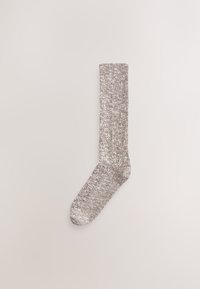 Chaussette en tricot beige clair avec un motif texturé, fabriquée dans un matériau doux et flexible, avec une hauteur standard à la cheville.