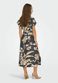 Cvećasta maksi haljina u tamnosivoj boji s bež uzorcima, kratkim rukavima, strukiranim pojasom i bočnim prorezima. U kombinaciji s bež visokim potpeticama.