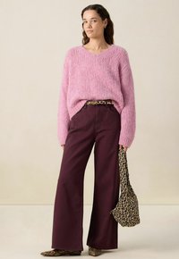 Pull en tricot épais rose avec un col en V, associé à un pantalon capri bordeaux à jambes larges. Accessoirisé avec une ceinture et un sac à imprimé léopard.