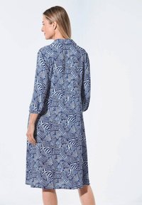 Langärmliges Kleid in Marineblau mit einem geometrischen weißen Muster. Verfügt über einen Kragen und Knopfdetails am Ausschnitt. Leichter Stoff.