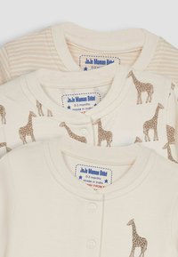 Set di tre articoli per neonati. Uno presenta un tessuto beige con stampa di giraffe; gli altri hanno righe crema. Tutti hanno chiusure a scatto e colli a coste.