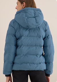 Niebieska puchowa kurtka z kapturem, pikowanym wzorem i elastycznymi mankietami. Gładka tekstura i dopasowany krój.