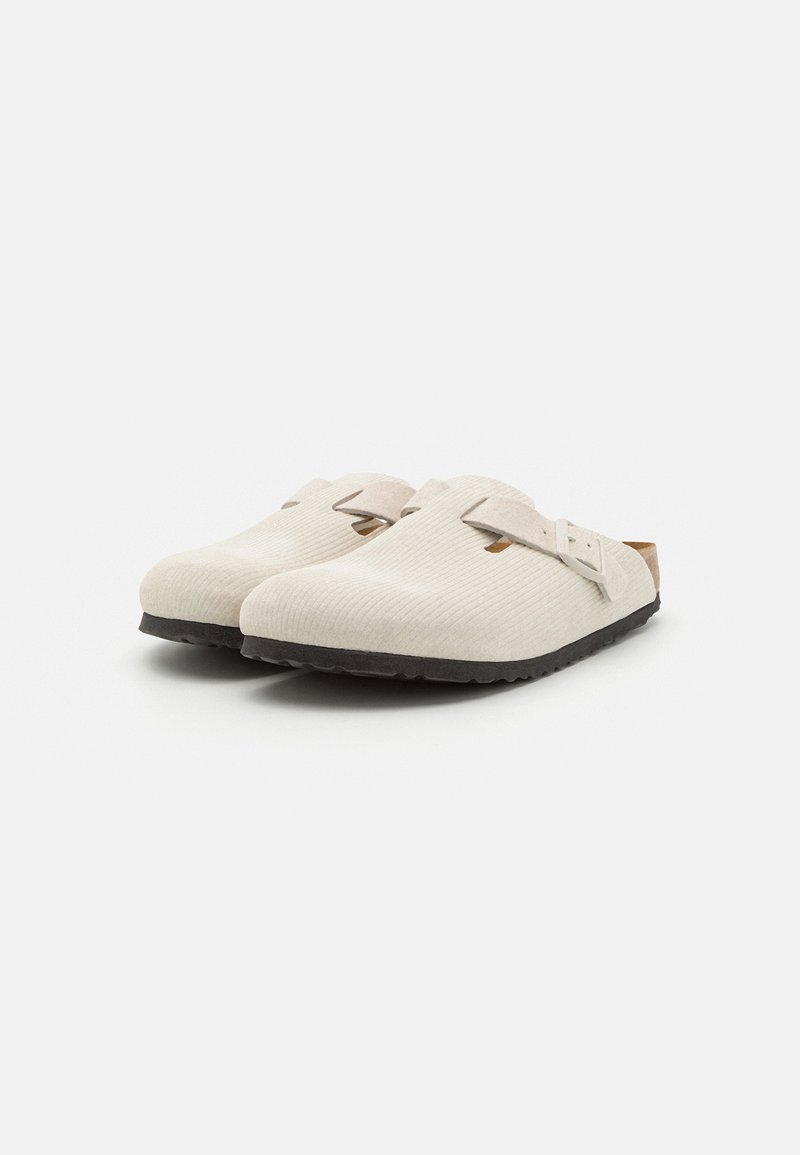 Beżowe klapki slip-on wykonane z teksturowanej tkaniny z czarnymi gumowymi podeszwami i regulowanym paskiem. Posiadają dwa wycięcia dla lepszej wentylacji.