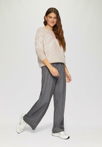 Hellrosa Pullover mit einem dezenten Muster, lockerer Passform und 3/4-Ärmeln, kombiniert mit grauen, hoch geschnittenen, weit geschnittenen Hosen und weißen Sneakers.