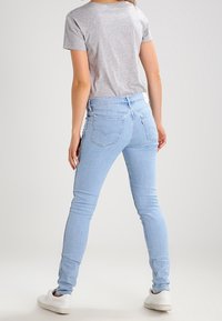 Jeans ajustados de color azul claro, fabricados en denim, con una cintura de altura media, bolsillos traseros y un acabado limpio. Combinados con una camiseta gris ajustada.