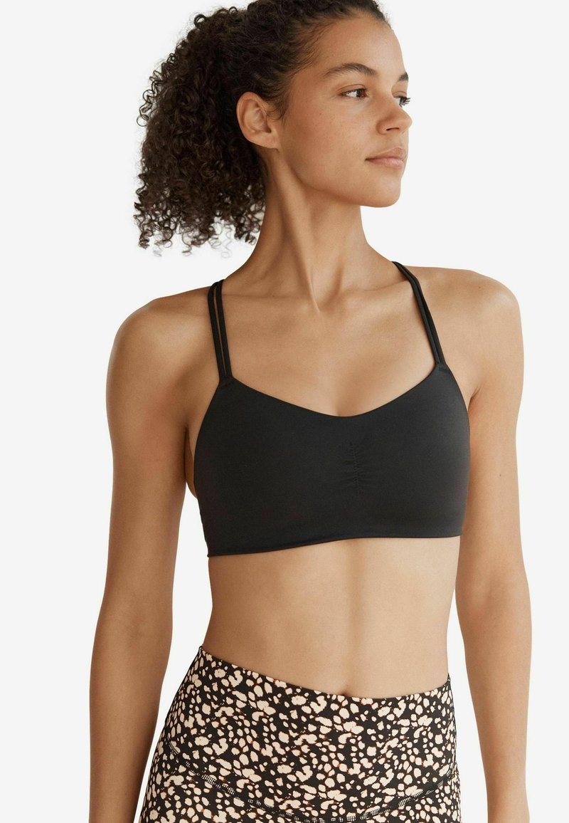 Brassiere sportivo nero con scollatura a V, caratterizzata da un centro arricciato e sottili spalline doppie. Indossato con leggings a vita alta a fantasia.
