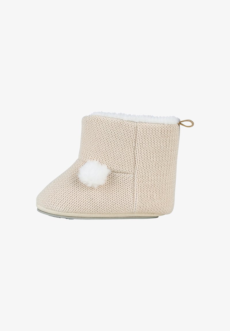 Chausson de bébé beige tricoté avec une doublure en fourrure blanche, un pompon duveteux sur le côté et une petite boucle à l'arrière pour un enfilage facile.