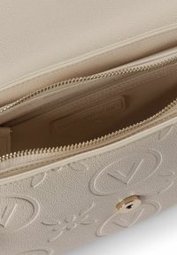 Borsa in pelle beige con texture, dettagli logo in rilievo, chiusura con zip e finiture in metallo color oro. Interno con fodera e etichetta.