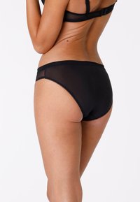 Perizoma nero trasparente con una texture liscia, caratterizzato da bordi ondulati e un design a vita media, che offre una copertura completa sul retro.