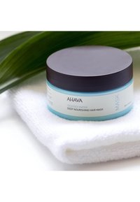 Maseczka do włosów AHAVA Deadsea Water Deep Nourishing w okrągłym pojemniku z czarną pokrywką, jasnoniebieskim paskiem i białą etykietą, umieszczona na białym ręczniku.