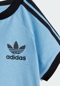 T-shirt azzurro chiaro con colletto e strisce nere. Presenta un logo ricamato nero. Realizzato in morbido tessuto misto cotone. Maniche corte.