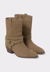 Las botas de tobillo de ante en tono marrón presentan una punta afilada, costados estructurados y una correa decorativa adornada con tachuelas plateadas y un acento de hardware circular.