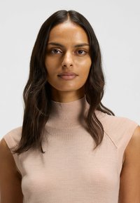 Beige sleeveless top with a high ribbed neckline, soft texture, and subtle stitch detailing on shoulders, displayed against a neutral background.