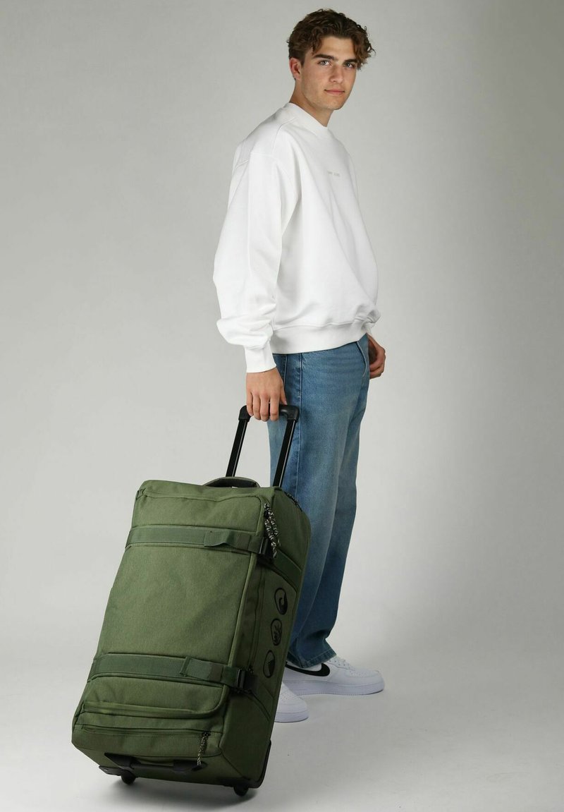 Borsa da viaggio verde con ruote realizzata in tessuto resistente, dotata di numerosi zip, dettagli con cinghie e manico estensibile. Design semplice.