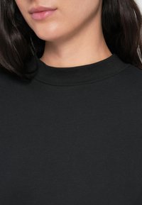 Top preto com gola simulada feito de tecido suave. Design justo ao corpo, textura simples sem padrões ou adornos.