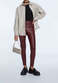 Camicia oversize beige con bottoni, top aderente nero, pantaloni in pelle bordeaux, borsa grigia con texture e mocassini neri con plateau.