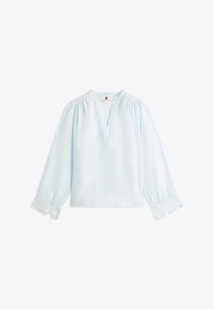 Lyseblå bluse med lange ermer, V-hals, rynkede skuldre og brede mansjetter, hver festet med en liten knapp.