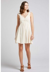 Robe couleur crème avec un corsage ajusté, des bretelles volantes et une jupe évasée. Fabriquée en tissu texturé avec un motif à carreaux subtil.