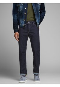 Mörkblå denimjeans med rak skärning och upprullade fickor, tillsammans med en mörkblå denimjacka och grå sneakers.